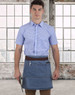 A denim half apron with a brown waistband, worn by a person in a blue checked shirt, against a city skyline backdrop.