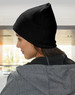 A beige cable knit beanie with a fleece headband, worn on a person’s head, seen from the side.