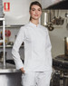 A white ladies' functional chef jacket displayed on a model in a professional kitchen setting. The jacket has a logo.