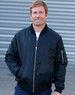A man in a black soft shell jacket with a zip-up front and side pockets, standing against a grey background.