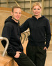 A navy full-zip fleecy hoodie with a logo, worn by a man and a woman in an indoor setting.