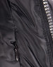 A close-up of a heavy quilted black puffer jacket featuring a zip and a side pocket. It has a logo on the front.
