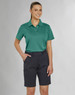 A woman in a teal polo shirt and navy utility cargo shorts, standing confidently with hands in pockets.