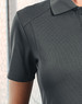 A grey polo shirt with a textured fabric and a collar, featuring a subtle logo.