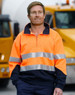 Hi-Vis long-sleeve fleece collar sweater in orange with reflective strips, paired with navy trousers. Features branding.