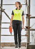 A woman is walking on scaffolding, wearing a yellow and black polo shirt and black cargo pants with a tool in hand.