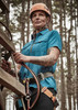 A woman wearing a blue short sleeve outdoor shirt with a harness, set against a forest background.