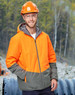 A Hi-Vis quilted two-tone safety jacket in orange and grey, worn by a man in a hard hat and safety glasses, outdoors.