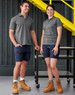 A pair of models wear unisex cotton stretch ripstop work shorts in navy, paired with grey polo shirts and work boots.