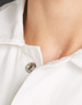 A close-up view of a white collared garment showing a button detail near the neckline. It has a logo.