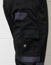 A close-up of black cargo pants featuring grey accents and a logo on the side.
