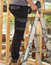 A pair of black work pants with grey accents, featuring pockets, being worn by a person on a ladder.