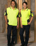 Two individuals stand in high-visibility yellow safety polo shirts with navy accents, inside an unfinished building.