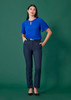 A woman standing in navy tapered pants with an adjustable waist, paired with a blue top, on a green background.