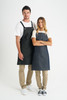 A pair of denim bib aprons in dark blue, worn by a man and a woman, featuring adjustable straps and pockets.