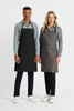 A black and a grey bib apron are displayed on two models, with each wearing a collared shirt and pants.