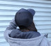 A black trucker cap with a mesh back, worn by a person in a grey hoodie. The background features a blue-grey wall.