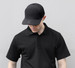 A black polyester/mesh cap with a logo, worn by a person in a matching black polo shirt.