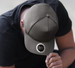 A grey cap with a round logo, resting on the head of a person wearing a black shirt.