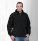 A man wearing a black polar fleece pullover with a half zip, standing against a light wooden background.