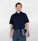 A man wearing a navy Dri Gear Summit Coolmax polo, paired with dark trousers and holding a tablet, stands against a neutral background.