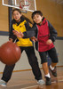 A boy in a red rain jacket and a girl in a yellow rain jacket play basketball indoors. Both jackets have branding.