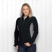 A woman models a black and grey soft shell jacket with zip pockets and a logo on the chest.