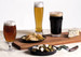 A craft beer glass set featuring three different beers: a dark stout, a pale lager, and an amber ale, alongside snacks.