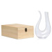A clear glass wine decanter with a unique shape beside a wooden box.