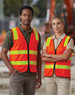 A high-visibility safety vest in bright orange with reflective strips, worn by two individuals on a construction site.