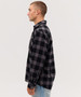A man in a black and grey checkered flannel long sleeve shirt, standing sideways against a plain background.