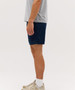A person wearing navy sports shorts, standing sideways, with a grey shirt and beige sneakers. The shorts feature a logo.
