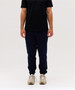 Navy track pants worn with a black t-shirt, featuring a fitted style and elasticised cuffs. The model wears beige sneakers.