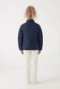 A puffer jacket in navy blue, viewed from the back, worn with light-coloured trousers. The jacket features a logo.