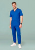 A man in a blue scrub top and slim leg jogger scrub pants, wearing white sneakers, standing against a green background.