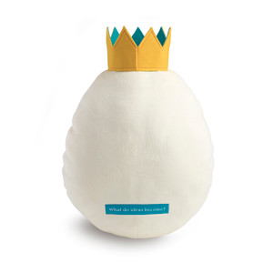 Back view of the "Idea" plush large white egg with a yellow crown with orange legs and feet. A label across its back reads, "What do ideas become?"
