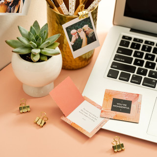Image shows a You're WonderfulThoughtFulls card, a contemporary pink, orange design, sitting on a laptop. Each card has an uplifting surprise quote on the inside, like a fortune cookie. 