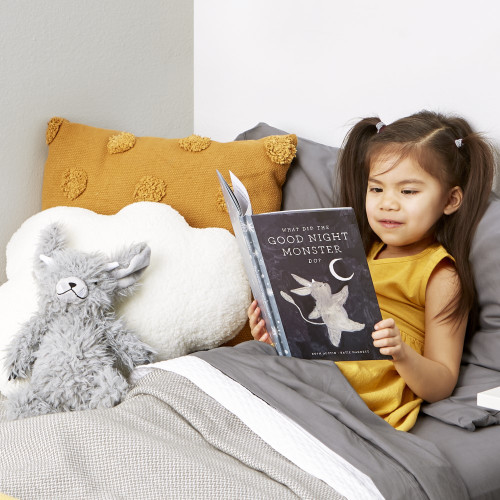 A photo of a young child reading Good Night Monster and holding her monster plush before going to bed. 