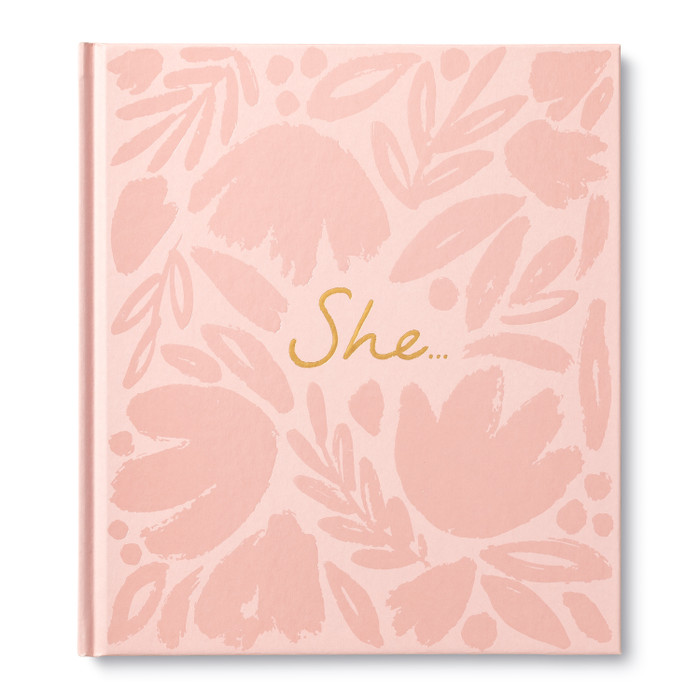 The front cover of inspiring friendship, women empowerment gift book, "She...", written by Kobi Yamada. The cover is pink with a floral pattern and the title "She..."{ embossed in gold foil.