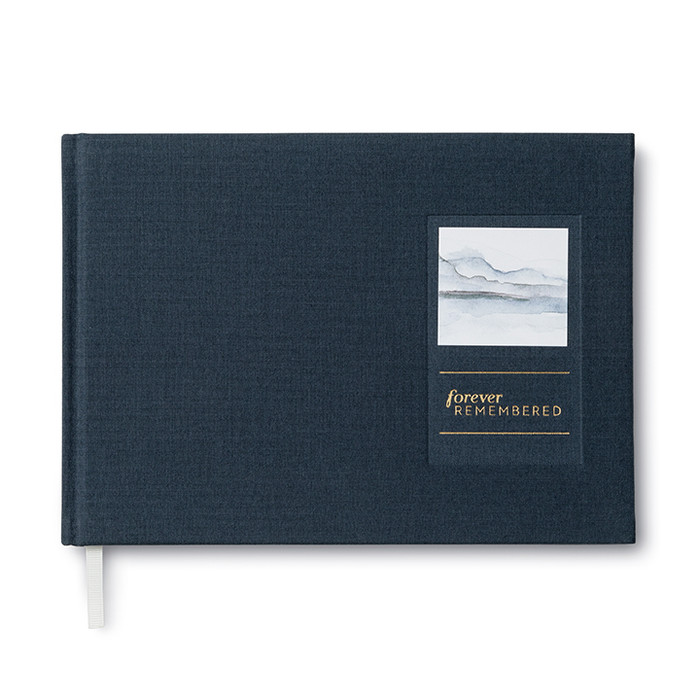 Front cover of "Forever Remembered, a memorial guest book". The cover is dark blue and has a debossed rectangle with a watercolor design that is white, light blue, and grey and the copy"Forever emembered" in gold foil placed below it.