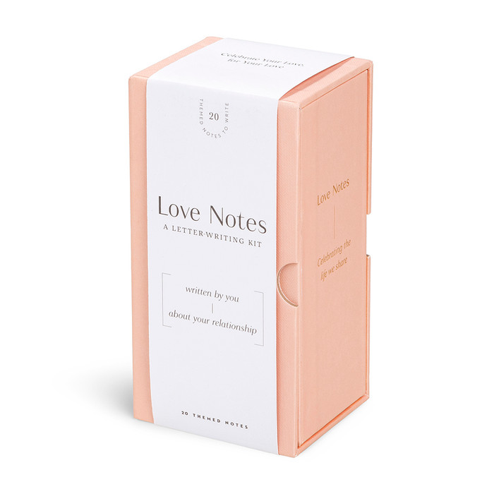 This image shows a front, angled view of the letter writing kit "Love Notes: Written by you, about your relationship". The kit is packaged in a keepsake light pink box with gold foil features. 
