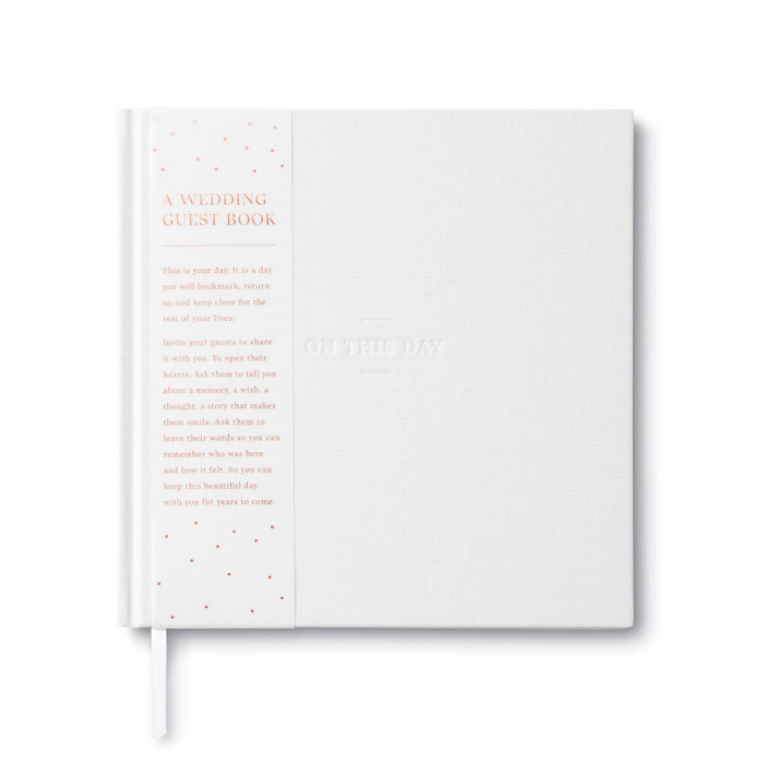 The cover of the wedding guest book, "On this Day". The cover is cloth white with the title debossed. A removeable belly band sleeve has a short description that reads, "A Wedding Guest Book. This is your day. It is a day you will bookmark, return to, and keep close for the rest of your lives. Invite your guests to share it with you. To open their hearts. Ask them to tell you about a memory, a wish, a thought, a story that makes them smile. Ask them to leave their words so you can remember who was here and how it felt. So you can keep this beautiful day with you for years to come."