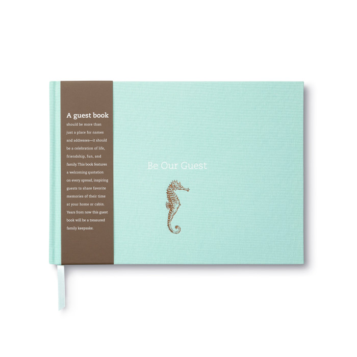 The front cover of the guest book, "Be Our Guest". The cover is teal with a gold foiled seahorse and the title "Be Our Guest" embossed in white. There's a removeable bellyband with a description of the book that reads: "A guest book should be more than just a place for names and addresses -- it should be a celebration of life, friendship, fun, and family. This book features a welcoming quotation on every spread, inspiring guests to share favorite memories of their time at your home or cabin. Years from now this guest book will be a treasured family keepsake."