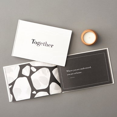 Lifestyle photo of the gift book, "Together". Book is open to a page that reads "Where you are understood, you are home."