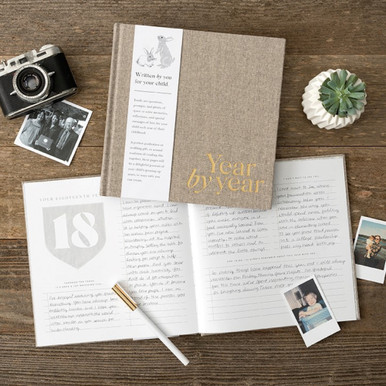 A photo of "Year by Year", a keepsake memory book to write a letter a year to your child from ages 1 to 18. A page from the book is open to age 18 and shows prompts to help you reflect and write thoughtful memories from that year.  