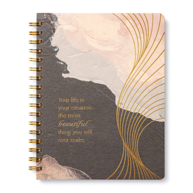 This image shows the front cover of a spiral notebook. The journal design features a pink, beige, and taupe background with gold foil accents. The statement on the cover reads, "Your Life Is Your Creation--the most beautiful thing you will ever make."