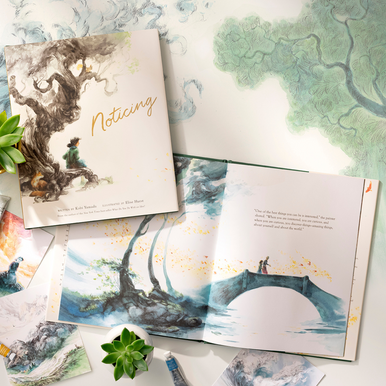 Lifestyle photo of the childrens book, Noticing, written by Kobi Yamada and illustrated by Elise Hurst. The book is open to a page that shows a girl and her artist mentor walking across a bridge, surrounded by birds and lovely trees along the riverbed. The copy on the page reads, "One of the best things you can be is interested," the painter shared. "When you are interested, you are curious, and when you are curious, you discover things-amazing things, about yourself, and about the world."