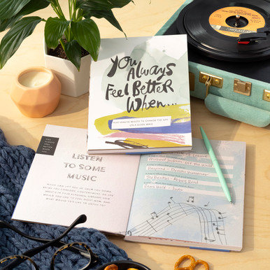 A lifestyle photo of the activity book "You Always Feel Better When..." The guided journal is open to a page that has the tite "Listen to some music" and has a record player in the background.