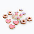 On white background there are 4 Pink frosted doughnuts, 6 pink and purple frosted sugar cookies, and 4 pink frosted mini cupcakes.