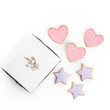 On white background there are 3 heart shaped sugar cookies with pink icing and 3 star shaped cookies with light purple icing and the square white bakery box embossed with the Queen's Treasures fleur-de-lis.
